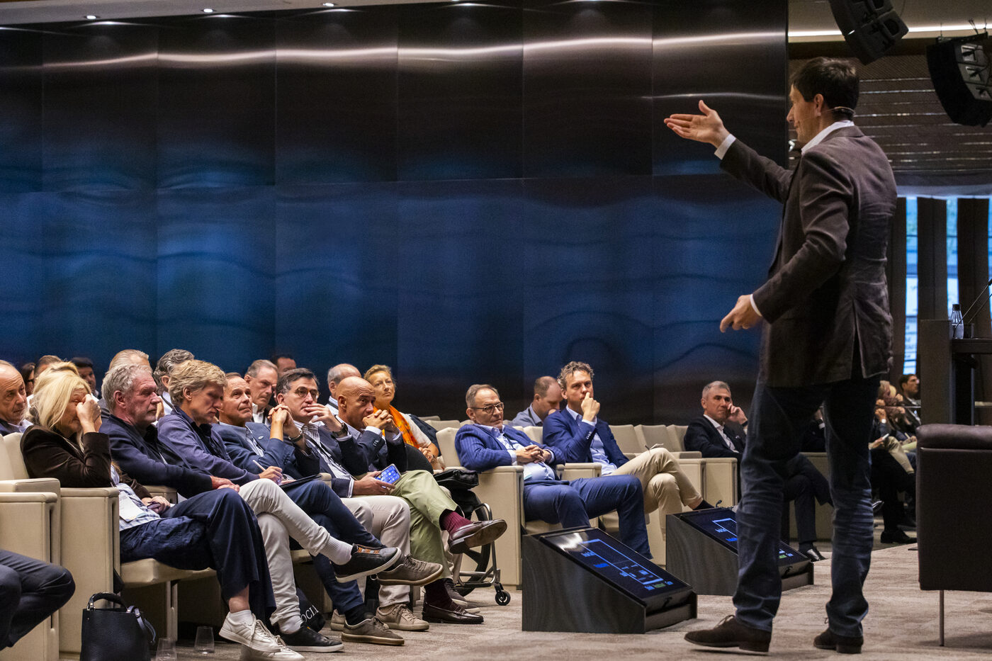 Chris speaking to a small room of leaders seated in a close semicircle, a dark blue wall behind him